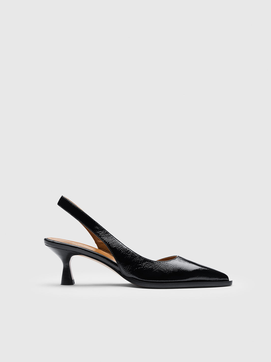 A black slingback shoe in shiny leather photographed against a light-gray studio background.