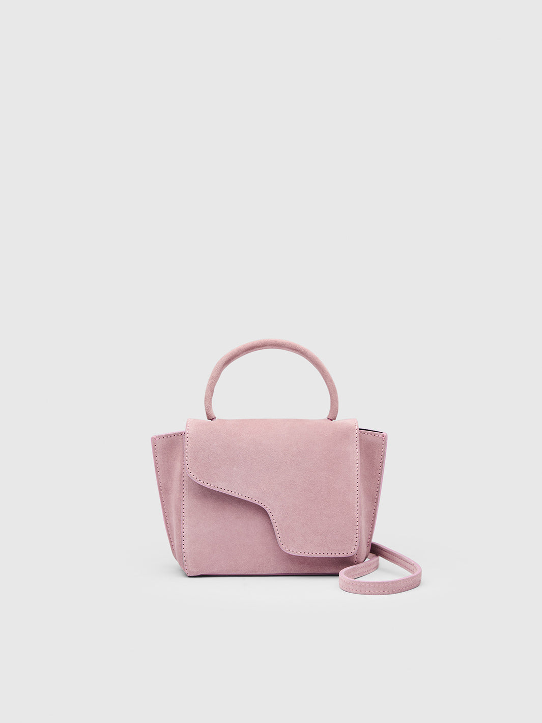 A small dusty pink suede handbag with a top handle and a matching shoulder strap, shown against a light gray background.