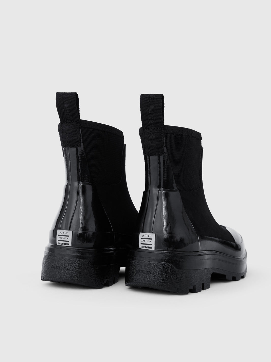 A pair of black Chelsea-style rubber ankle rain boots with elastic side panels, pull tabs, and thick lug soles.
